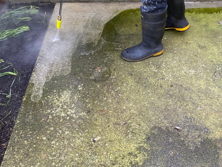 An area of cement walkway. A person wearing rubber boots is performing the power wash
