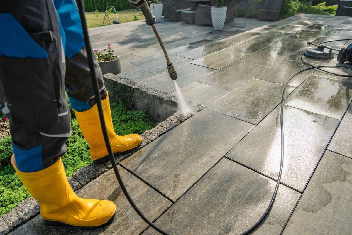 Worker using a pressure washer to clean a stone patio on a sunny day