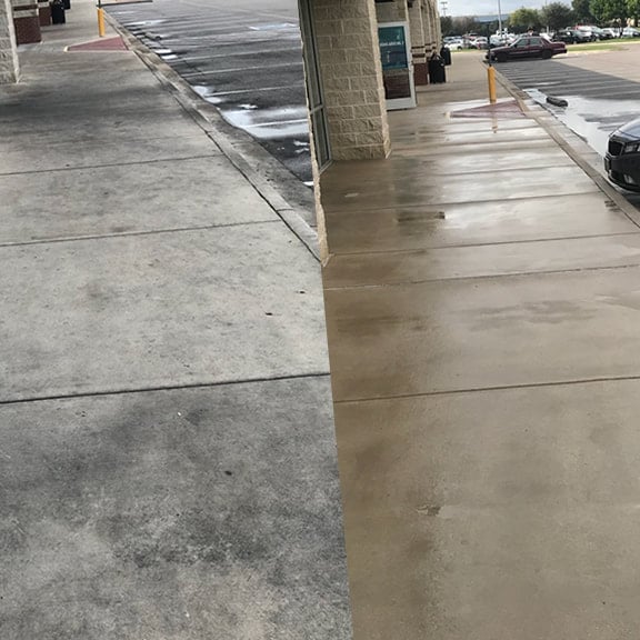 Before and after comparison of a concrete parking lot surface, with left side dry and right side wet, showing cleaning or washing results