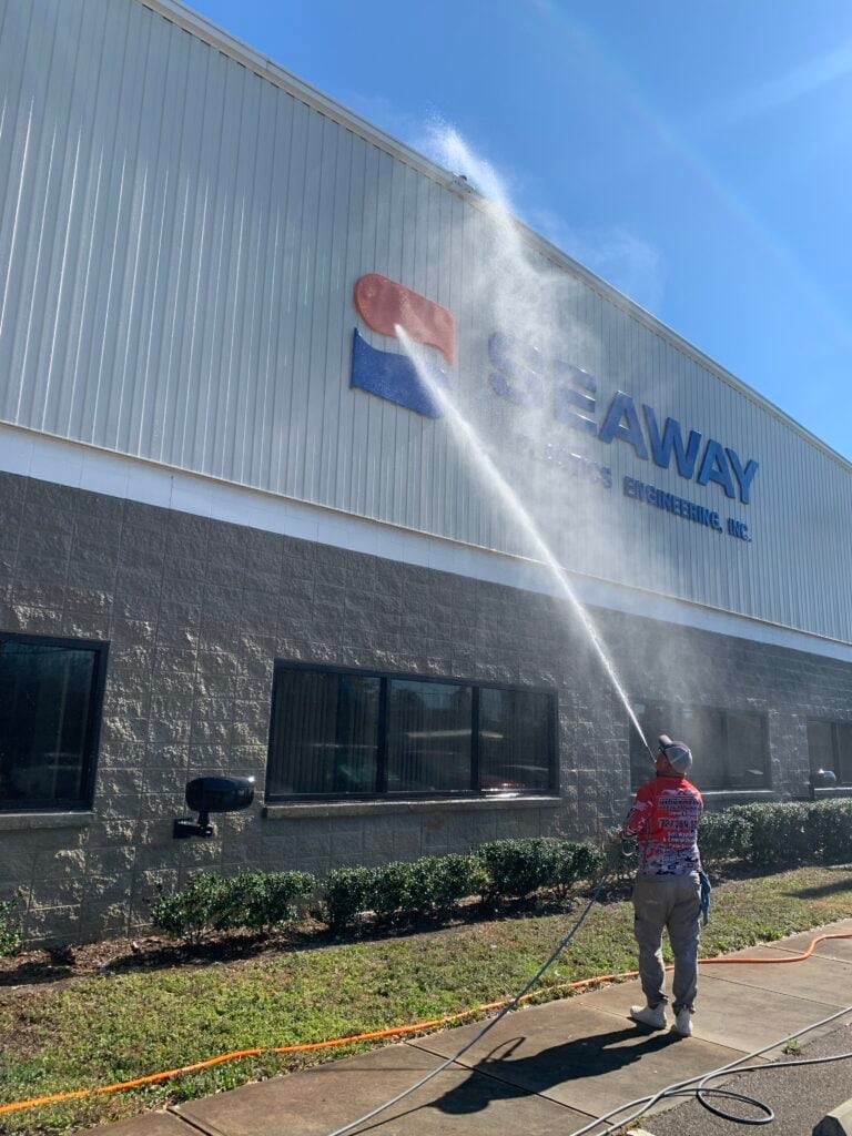 Worker spraying water on SeaWay building facade with pressure washer on sunny day