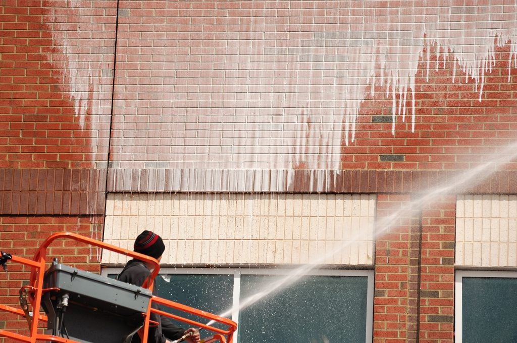 Worker on a lift spraying water on a brick building facade during cleaning or maintenance operations