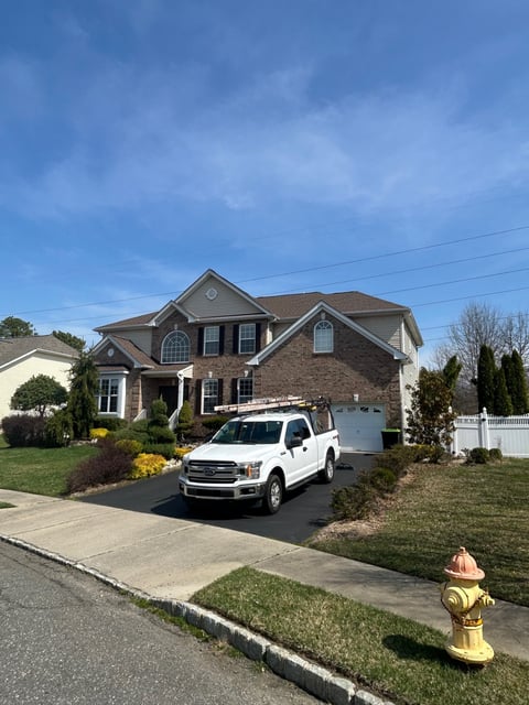 Two-story brick house with white trim, white pickup truck in driveway, manicured lawn, and fire hydrant in foreground